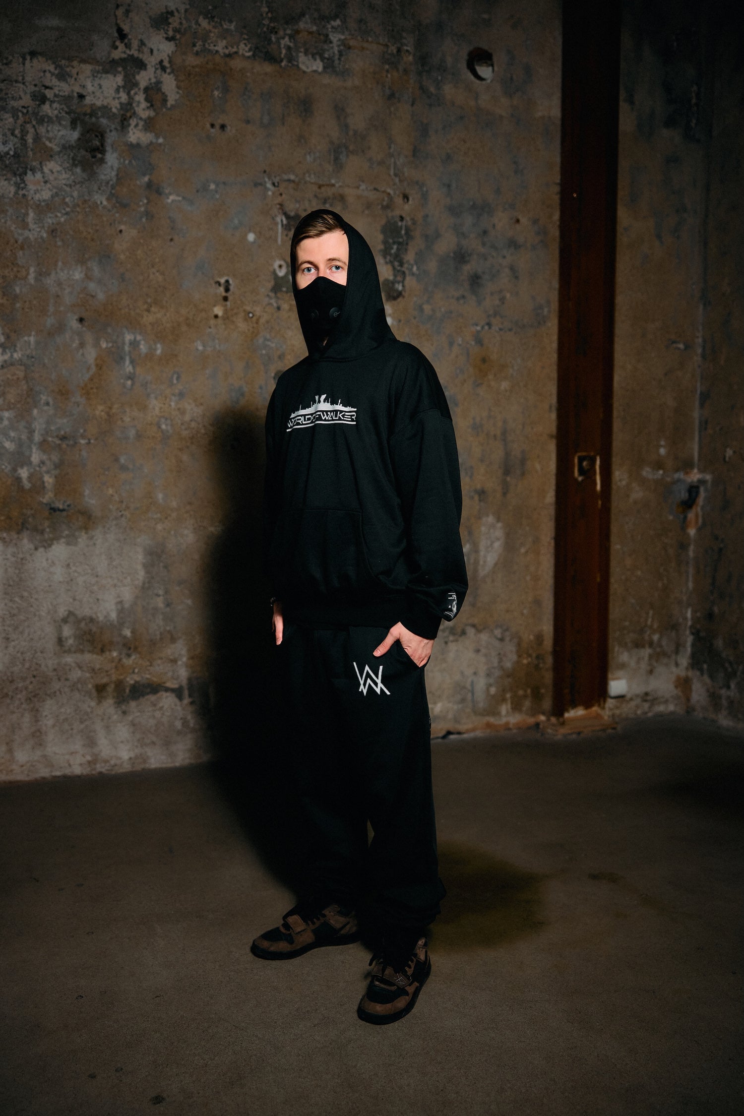 Person wearing a black hoodie with a logo in a dimly lit room.